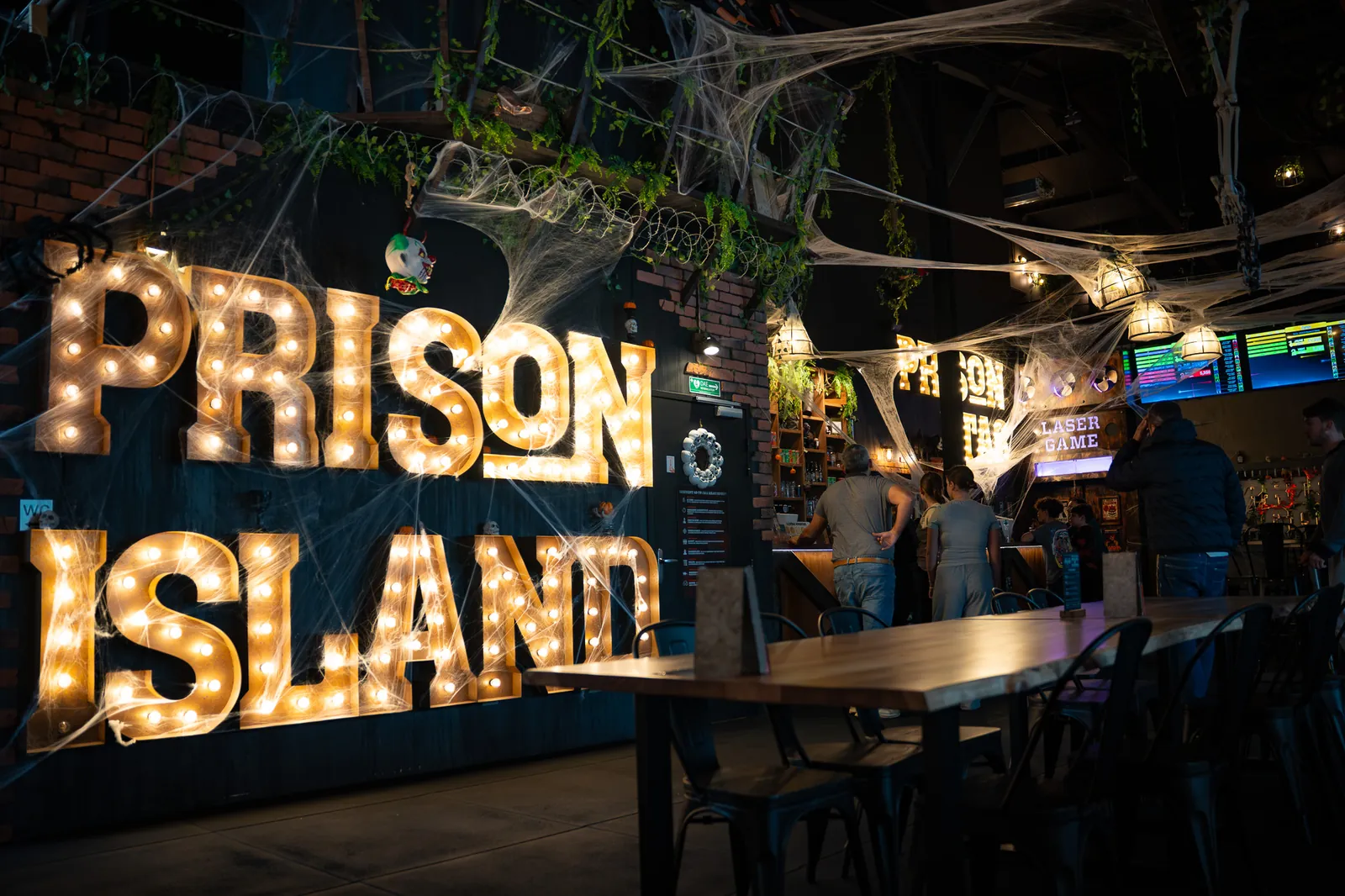 O bar por baixo do letreiro luminoso Prison Island, mesas de madeira em primeiro plano