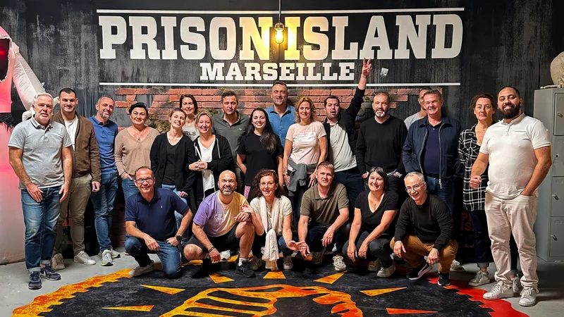 Umas trinta pessoas posam em duas filas diante do letreiro Prison Island Marseille, com o emblema pintado no chão